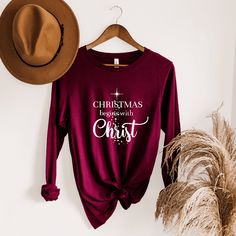 Enrich your wardrobe with this Christmas Begins with Christ Shirt. This long-sleeve Christmas tee is soft, and stylish and best of all shares a great reminder of the true reason for Christmas. It's sure to be your go-to Christmas shirt for everything from Christmas shopping to baking cookies and more. Pair it with jeans for a comfy casual Christian outfit, or layer it with a jacket for a classy winter fashion. It's versatile, soft and flattering for a variety of styles and occasions! This unisex Classy Winter Fashion, Christ Shirts, Christian Hats, Patriotic Outfit, Baking Cookies, Christian Sweatshirt, Christmas Tees, Christian Clothing, Mens Sweatshirts Hoodie