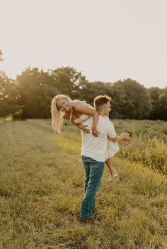 a man carrying a woman on his back in the middle of a field at sunset