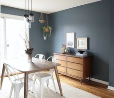 an empty dining room with blue walls and white chairs in the corner, next to a wooden table