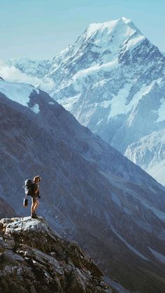 a man standing on top of a mountain next to a large snow covered mountain range