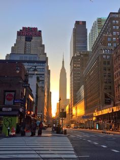 the sun is setting on a city street with tall buildings and skyscrapers in the background