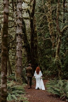 a bride and groom walking through the woods