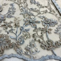 an embroidered fabric with silver flowers and beads on white background, closeup view from the bottom