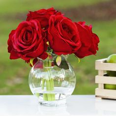 a vase filled with red roses sitting on top of a table next to an apple crate