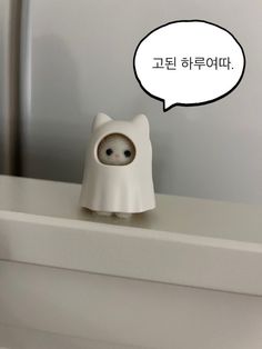 a white cat figurine sitting on top of a counter next to a speech bubble