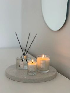 three candles sitting on top of a white counter in front of a mirror with black sticks sticking out of it