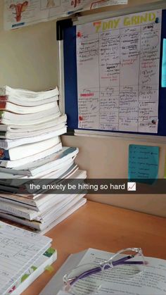 a pile of papers sitting on top of a desk next to a whiteboard with writing on it