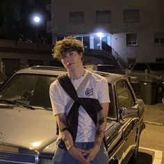 a young man sitting on the hood of a car in front of a building at night