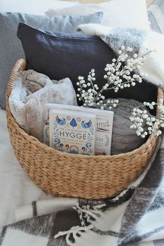 a basket filled with books and blankets on top of a bed next to a pillow