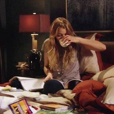 a woman sitting on top of a bed next to a book and cup filled with liquid