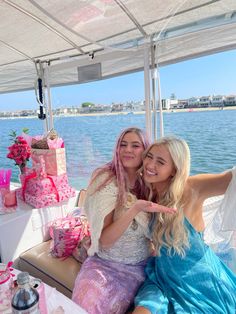 two beautiful women sitting on top of a boat next to each other in front of a cake