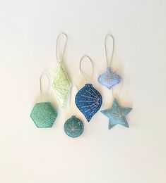 three ornaments are hanging from strings on a white surface, one is blue and the other is green