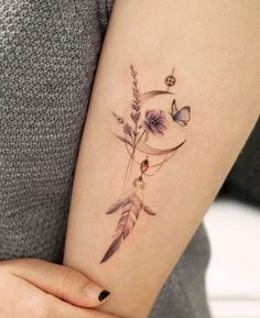 a woman's arm with a tattoo on it that has flowers and a crescent moon