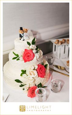 a wedding cake with roses and groom figurines on top, surrounded by cupcakes