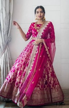 a woman in a pink lehenga standing next to a window with her hands on her hips