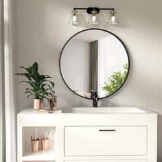 a bathroom vanity with a round mirror above it and potted plants on the counter