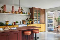 a kitchen with yellow cabinets and brown stools next to an open glass sliding door