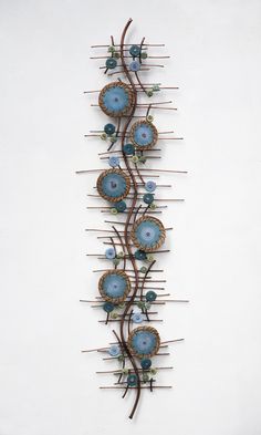 a metal wall sculpture with blue flowers and leaves on it's sides, against a white background