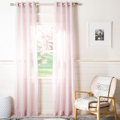 a chair and rug in front of a window with pink curtains on the windowsill