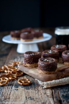 chocolate donuts and pretzels sitting on a wooden table next to some beer