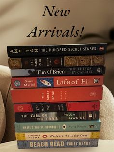 a stack of books sitting on top of a chair next to a white wall with the words new arrivals