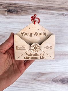 a hand holding an envelope with the word dear santa on it and a red ribbon