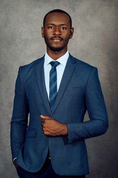 a man in a blue suit and tie posing for a photo with his hand on his hip