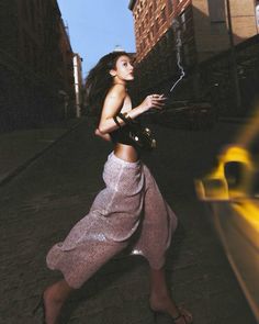 a woman is walking down the street with an umbrella in her hand and wearing a skirt