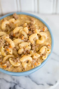 a blue bowl filled with macaroni and cheese on top of a marble counter