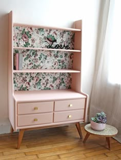 a pink dresser with floral wallpaper on it and a small potted succulent next to it