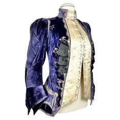 Circa 1905 Paris London Jacket with integrated waistcoat for an Amazon or for transvestism in the taste of the 18th century, designed by the famous Haute Couture House Gustave Beer during the Belle Epoque. Marquis’ suit, officer's collar, long sleeves with musketeer cuffs, in violet velvet densely embroidered with blades and silver thread. Complete with crenellated pockets and matching buttons, this suit opens onto two sides of an 18th century waistcoat in cream silk satin embroidered with silk, cannetilles and silver paillons. The waistcoat is fastened with hooks. A ruché of black satin ribbons decorates the front and pockets. The cream silk satin lining is partially incomplete due to the iron-laden, chemically perishable silks of the period. The numbered label 5394 (?) indicates Beer, 7 Vintage Outerwear With Epaulettes For Costume, Vintage Costume Outerwear With Epaulettes, Victorian Outerwear With Historical Design For Costume, Victorian Historical Outerwear For Costumes, Victorian Style Historical Costume Outerwear, Vintage Outerwear With Historical Design For Costume, Vintage Costume Outerwear With Historical Design, Antique Victorian Dress Costume With Historical Design, Antique Victorian Costume Dress With Historical Design