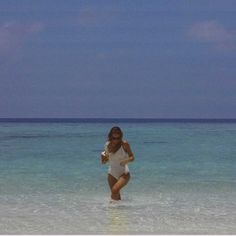 a woman in a white bodysuit is wading through the water at the beach