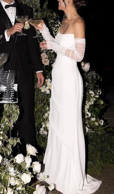 a man and woman standing next to each other holding wine glasses in front of flowers