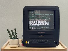 an old computer monitor sitting on top of a wooden table next to a potted plant