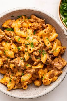 a bowl full of pasta with meat and cheese in it next to a plate of greens