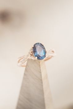 a blue diamond ring sitting on top of a wooden stand