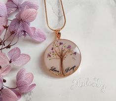 a glass pendant with a tree on it next to some purple flowers and pink leaves