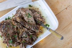 a white plate topped with meat and garnish on top of a wooden table