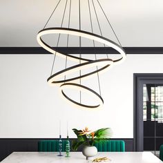 a modern chandelier hanging over a dining room table with green chairs and vases