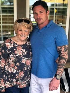 a man and woman standing next to each other in front of a house with tattoos on their arms