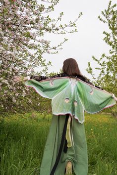 a woman in a green kimono with a large butterfly on her back, walking through the grass