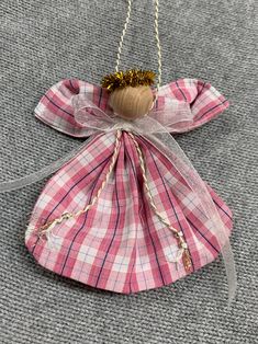 an angel ornament hanging from a chain on a carpeted floor with a pink checkered fabric