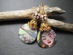 These earrings feature wonderful illustrated enameled copper charms by TheDreamCatchersCo in Bulgaria. One charm depicts a serene brunet girl with lilac flowers in her hair, while the other depicts the bucolic country view.  Above the charms are a double layer of soft pink enamel flower beads caps followed by ornate gold bead caps. Next are rhinestone spacers set in gold. These are topped by pink disco ball beads. Small brass beads finish off these bohemian country life earrings, which hang from simple gold ear wires and measure 2.25 inches long. These earrings will be sent to you attractively packaged in a gift box with ribbon. You can check out more of my one-of-a-kind creations here: http://www.etsy.com/shop/ThreeWishesStudio. Hand Painted Bohemian Enamel Jewelry, Bohemian Hand-painted Enamel Jewelry, Bohemian Hand Painted Enamel Jewelry, Whimsical Hand Painted Gold Earrings, Whimsical Enamel Jewelry For Jewelry Making, Bohemian Enamel Earrings For Gift, Whimsical Hand Painted Enamel Jewelry, Bohemian Hand Painted Gold Earrings, Bohemian Gold Hand Painted Earrings