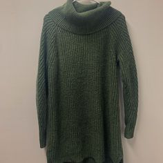 a green turtle neck sweater hanging on a white wall next to a coat hanger