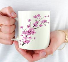 a woman holding a coffee mug with pink flowers painted on it