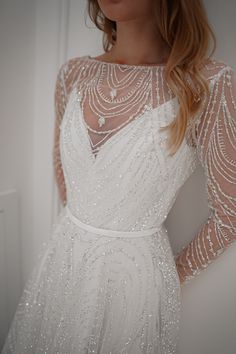 a woman is wearing a white dress with sheer sleeves and sequins on it