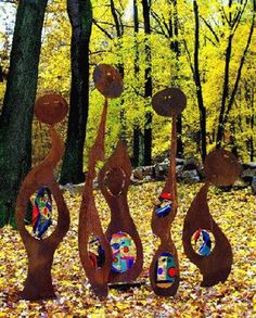 three metal sculptures in the woods with leaves on the ground