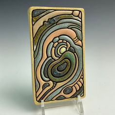 a decorative tile with an abstract design on the front and back side, sitting on a clear acrylic stand