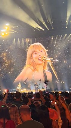 a woman singing into a microphone in front of a large screen with lights on it