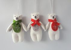 three white teddy bears hanging from strings with red bows and green ribbons on their backs